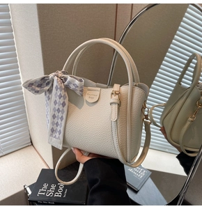 Detail of off-white lychee texture bucket bag with purple checkered bow and golden hardware