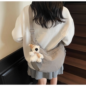 Close-up of grey crescent crossbody bag with cute teddy bear charm on wooden stairs