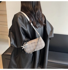 Detail of grey checkered crossbody bag with silver chain and rabbit charm on leather seat