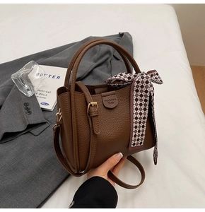 Detail of dark brown leather bucket bag with fashion embossing and checkered silk scarf