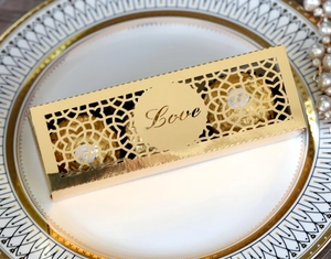 Goldene lasergeschnittene Love-Hochzeitsbox auf Porzellanteller mit Schokolade