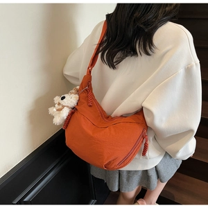Orange nylon half-moon crossbody bag with a cute plush dog pendant shown on a model