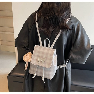 Détail d'un sac à dos à carreaux gris avec un papillon argenté et un pendentif ours en peluche