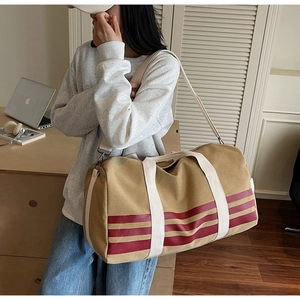 Large khaki canvas travel bag with red stripes worn by model in a cozy indoor setting