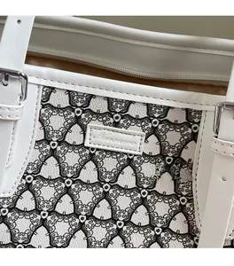 Detail of white leather tote bag with geometric patterns and metallic brand plate