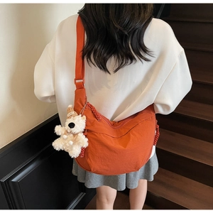 Close-up of orange crescent nylon crossbody bag featuring a cute white plush bear charm