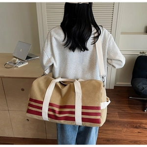 Detail view of khaki canvas duffel bag with red stripes worn by model in home setting