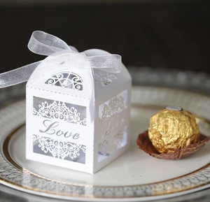 Macro shot of white laser-cut Love candy box with organza ribbon on elegant dinner plate