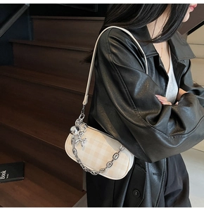 Detail of cream plaid shoulder bag with silver chain and unique doll pendant decoration