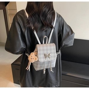 Détail du sac à dos à carreaux gris avec boucle papillon et breloque ours en peluche