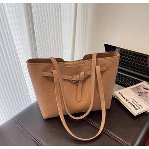 Close-up of caramel tote bag with pebble leather texture and buckle detail on a bench