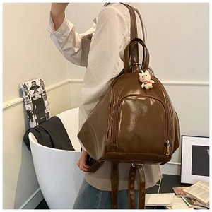 Detail view of a glossy dark brown tote backpack featuring a lucky cat charm decoration