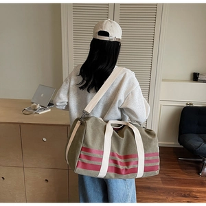 Olive canvas travel bag with red stripes and shoulder strap shown on a model