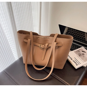 Detail of khaki pebbled leather tote bag with gold buckle on a professional desk
