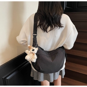 Detail view of large black crescent crossbody bag with cute white plush bear charm