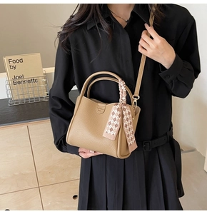Detailed view of a tan leather bucket bag with a decorative silk scarf on the handle