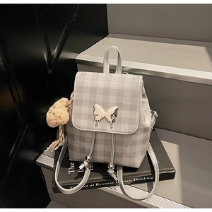 Détail d'un mini sac à dos à carreaux gris avec fermoir papillon et breloque ourson