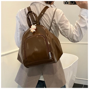 Brown patent leather backpack with white rabbit charm shown on a female model