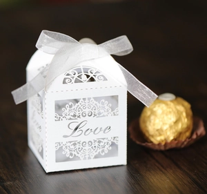 Detailed view of white laser-cut LOVE wedding candy box with a ribbon on wooden surface