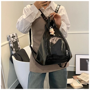 Glossy black triangular backpack with cat plush charm and zipper pocket detail