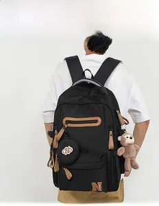 Detailed back view of a black high-capacity backpack with plush monkey and round pouch charm