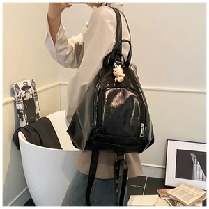Glossy black backpack with metallic zippers and cat plush pendant shown in lifestyle setting