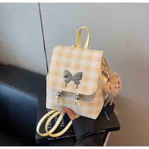 Gros plan du sac à dos à carreaux jaunes avec ornement papillon et charme d'ours