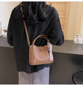 Detail of brown litchi leather bucket bag featuring a decorative scarf and shoulder strap