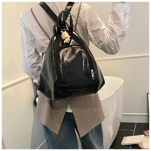 Detailed view of shiny black patent leather backpack featuring a cute white rabbit pendant