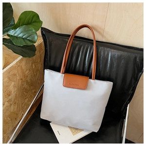 Detail of grey tote bag with brown leather handles and brand logo on a leather chair