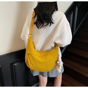 Detail of yellow nylon dumpling bag with adjustable strap and plush pendant on model