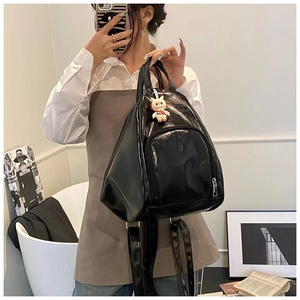 Detail of black patent leather tote bag featuring a glossy finish and astronaut pendant