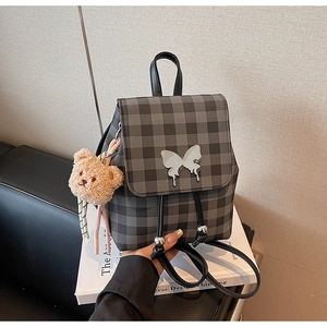 Détail d'un mini sac à dos à carreaux gris avec papillon métallique et breloque ourson