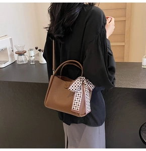 Close-up of brown pebbled leather handbag with checkered scarf on a cafe counter