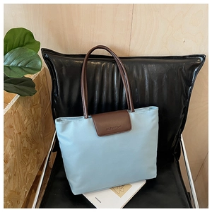 Detail of light blue tote bag with brown straps and CLEAROK logo on a black chair