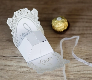 Detailed laser-cut white wedding favor box featuring LOVE script on wooden background