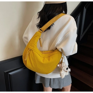 Detail of yellow nylon dumpling bag featuring a wide strap and a cute plush dog charm