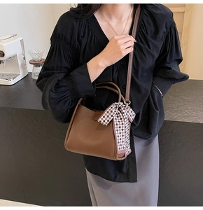 Close-up of brown litchi pattern leather bucket bag with silk scarf detail and shoulder strap