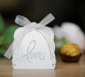Detail of white laser-cut Love wedding favor box with a delicate ribbon bow on wood