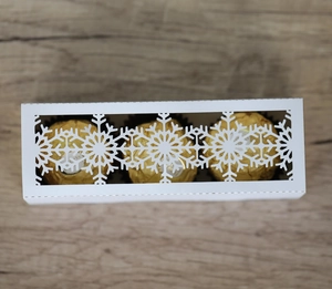 Macro shot of white cutout snowflake paper box holding three chocolate truffles