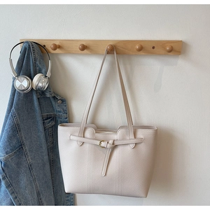 Detail of cream white tote bag with lychee grain texture and metal buckle hanging on rack