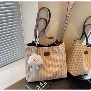 Detail of V-weave straw tote bag with brown leather straps and cloud plush charm accessory
