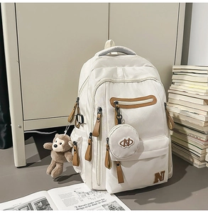 Close-up of beige nylon backpack with multi-pockets, leather details and plush monkey charm