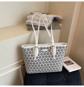 Close-up of a white tote bag with black geometric patterns and leather straps on a stool