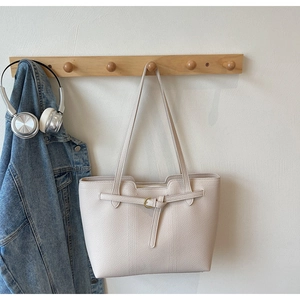 Detail of cream pebbled leather tote bag hanging with gold buckle and zipper closure