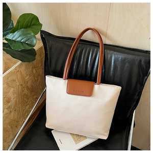 Detailed shot of a beige tote bag with brown leather straps and metal buckle closure