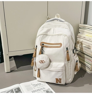 Detail of cream canvas backpack featuring leather zipper pulls and small coin purse charm