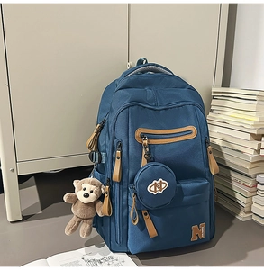 Detail of navy canvas backpack with leather pulls and a small plush monkey charm accessory