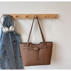 Close-up of brown litchi pattern tote bag hanging on wooden hook with blue denim jacket