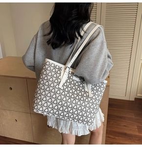 Close-up of a large black and white geometric tote bag with white shoulder strap on a model